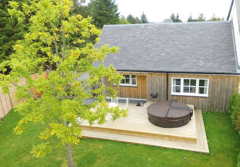 Modern single-storey wooden cottage with decked patio, hot tub, and manicured garden