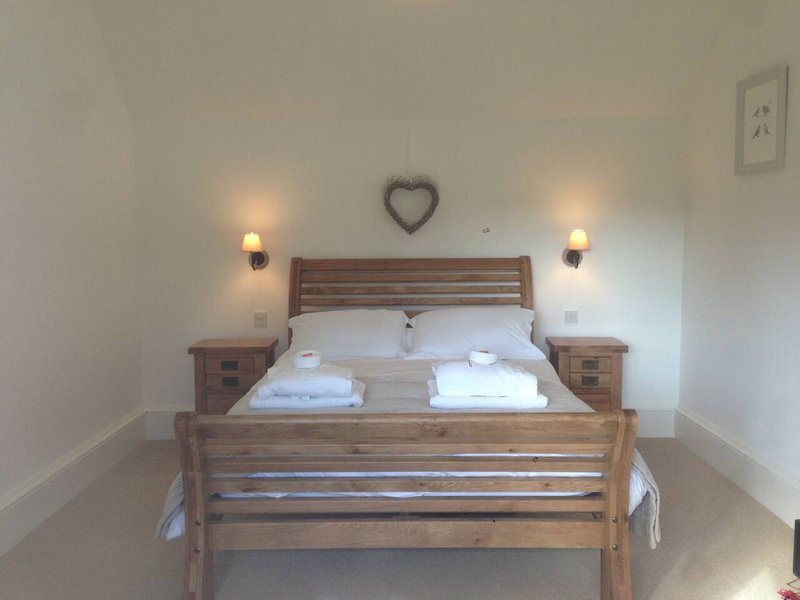Bedroom with wooden bed frame, white bedding, two nightstands, wall sconces and heart decoration