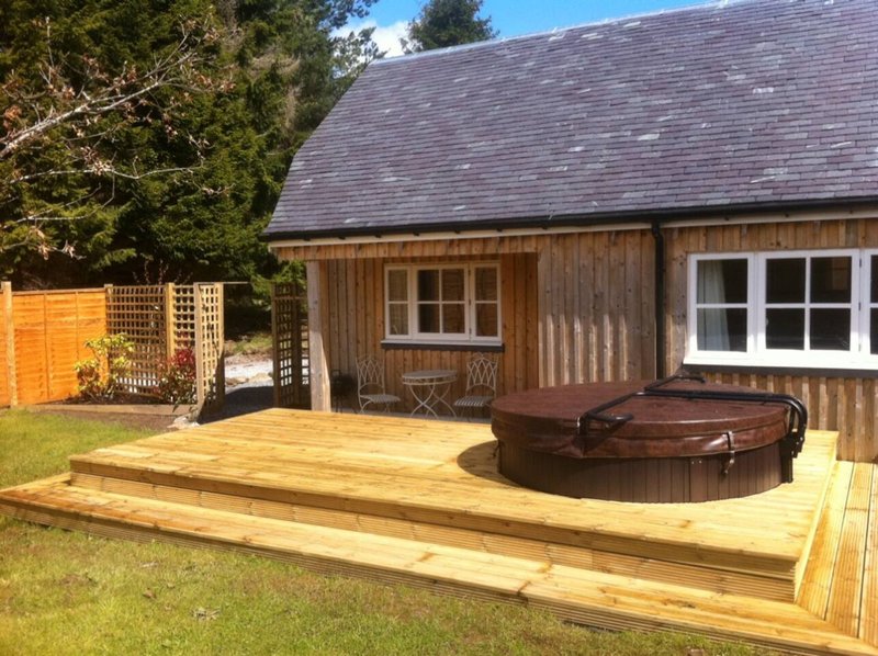 Wooden cabin exterior with decking, hot tub, garden fence and lawn