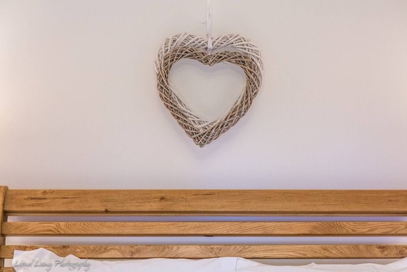 Pale wall with woven heart decoration and wooden shelf below