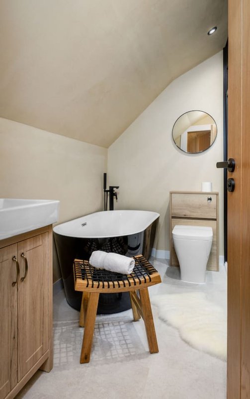 Modern bathroom with black and white soaker tub, wooden vanity, toilet, and circular mirror