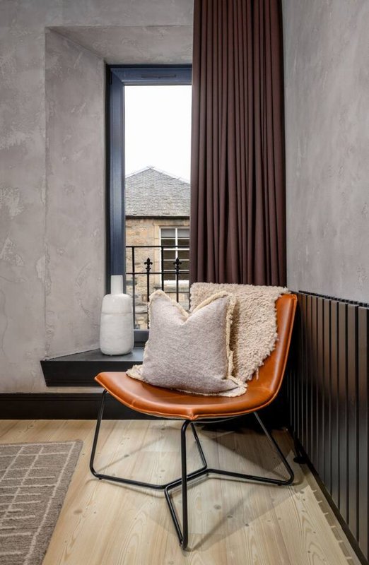 Modern seating nook with orange leather chair, cushions, and view through window to rooftop