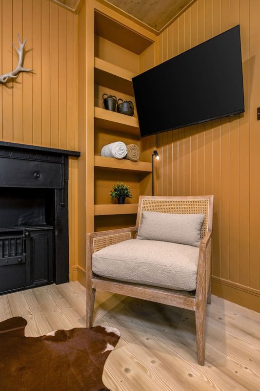 Cozy living room corner with wooden chair, fireplace, shelving, and mounted TV