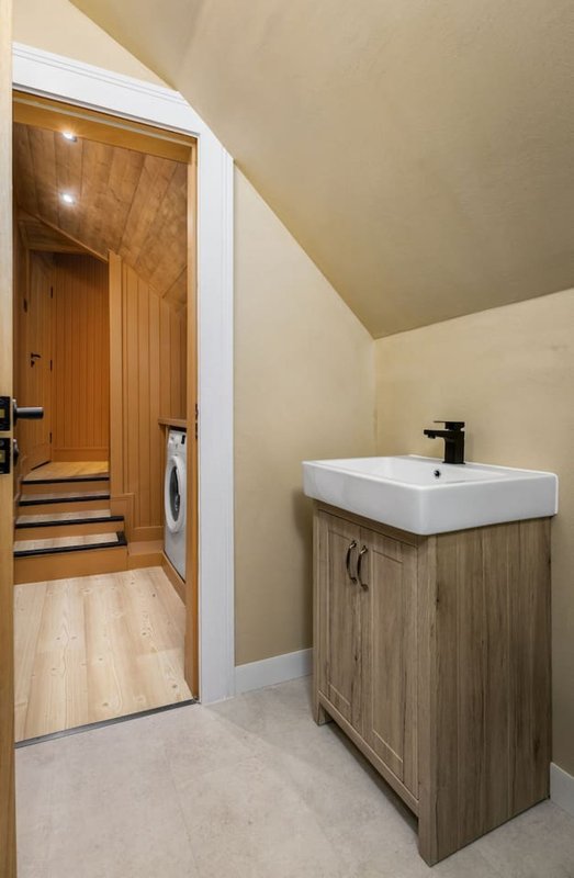 Modern bathroom with vanity sink, wooden cabinetry, and view into hallway with washing machine