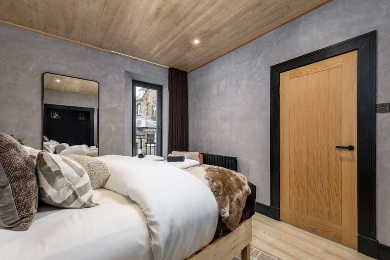 Modern bedroom with double bed, decorative pillows, wooden door and mirror
