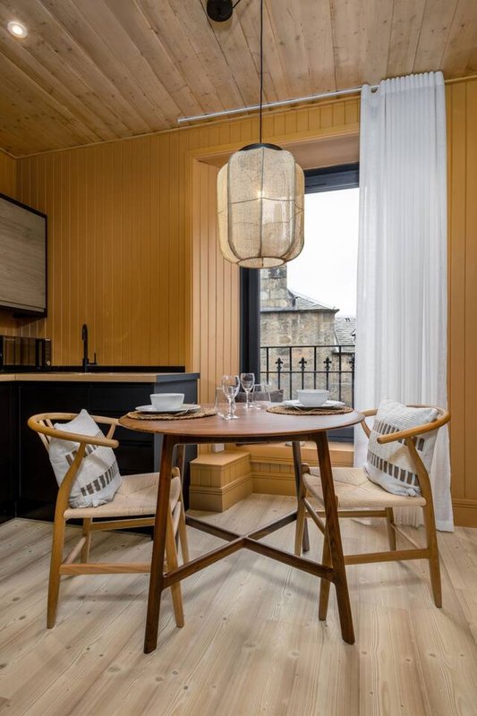 Modern dining area with wooden table, woven chairs, pendant lamp and city views through large window