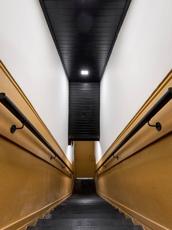 Narrow corridor with golden-yellow walls, black ceiling, and metal handrails on both sides
