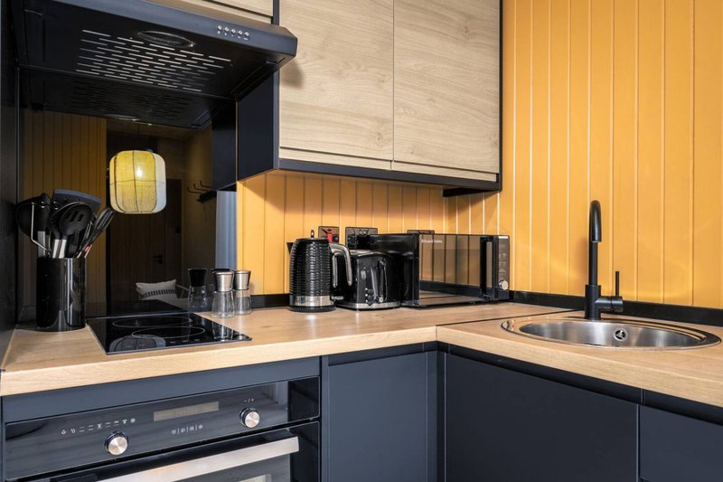 Modern kitchen with dark cabinetry, light wood countertop, black cooker and sink