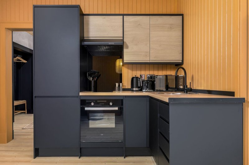 Modern kitchen with dark cabinetry, wooden countertop, integrated appliances and orange-striped walls