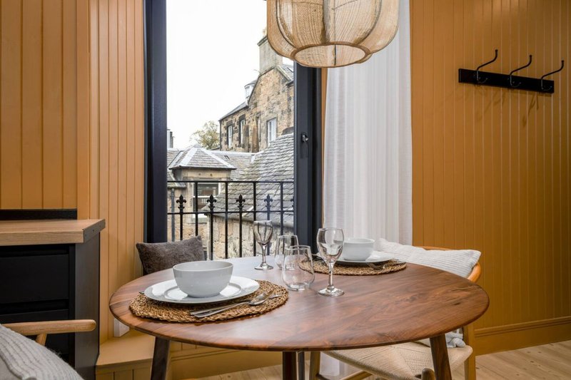 Dining table set for two with woven placemats, balcony overlooking stone building and rooftop