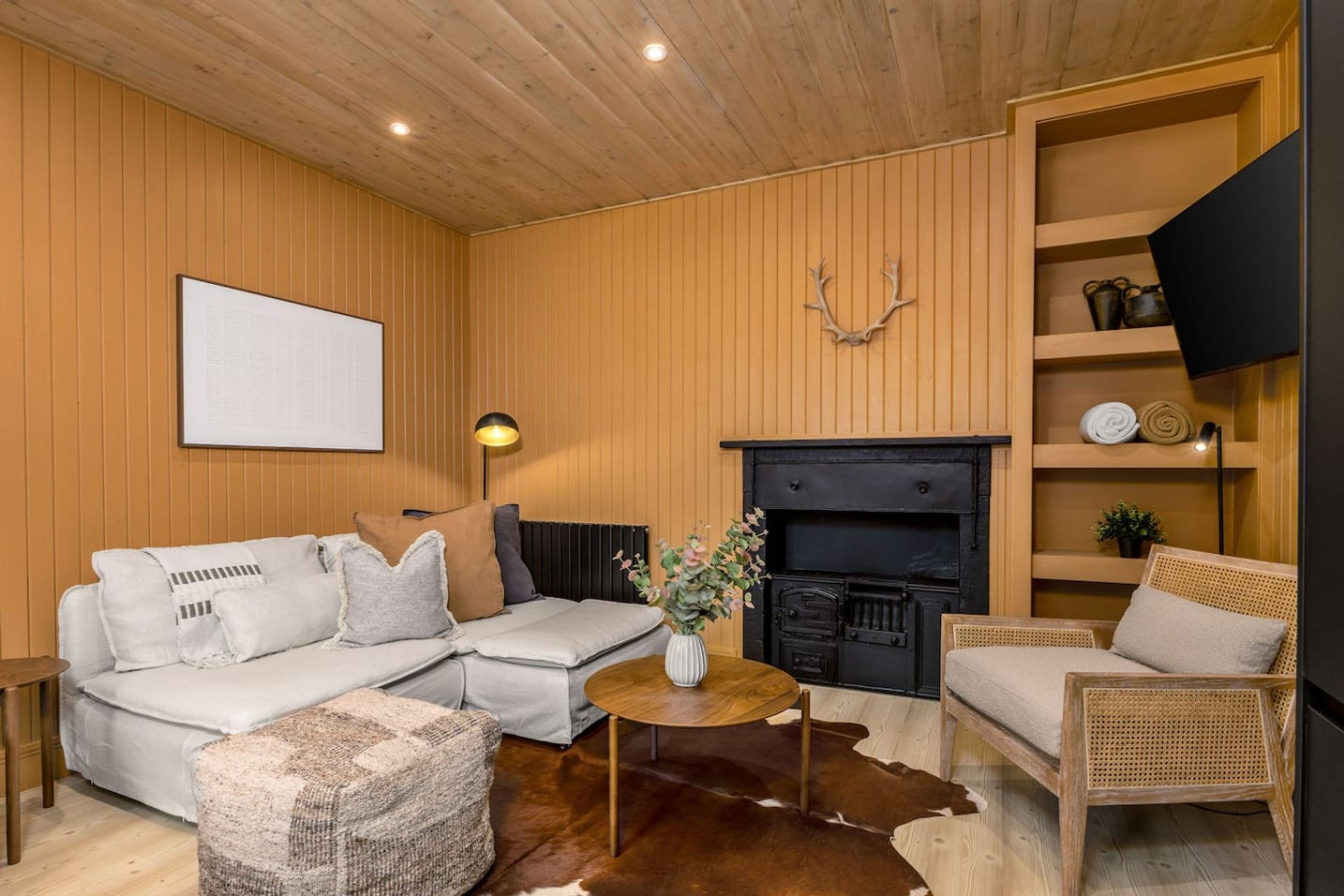Wooden cabin interior with cream sofa, fireplace, armchair and built-in shelving