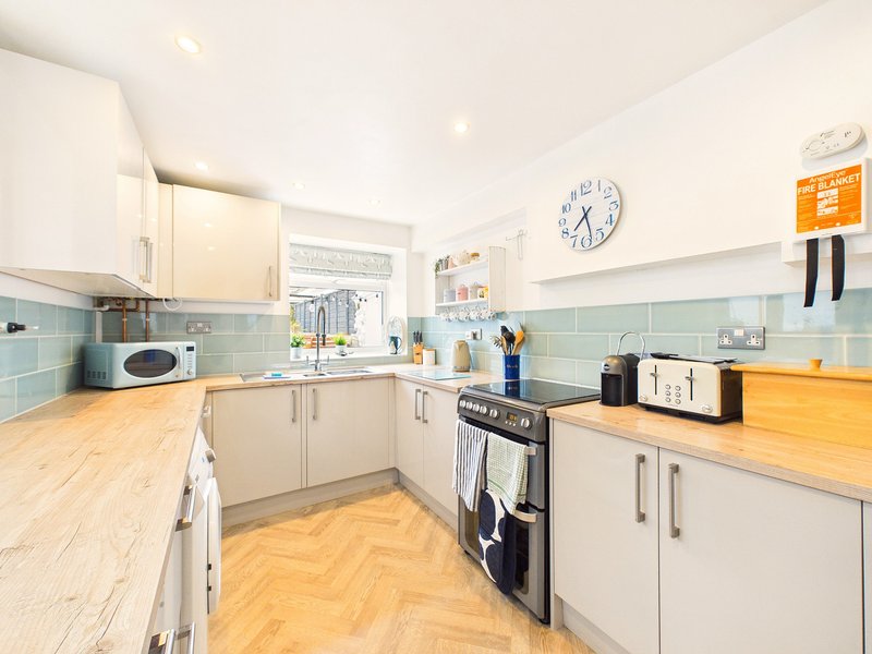 Bright modern kitchen with cream cabinets, wooden countertops, black range cooker and mint tile splashback