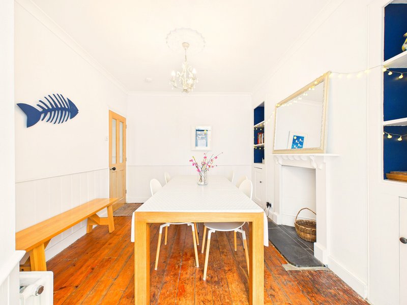Bright dining room with wooden table, white chairs, hardwood floor and blue wall art