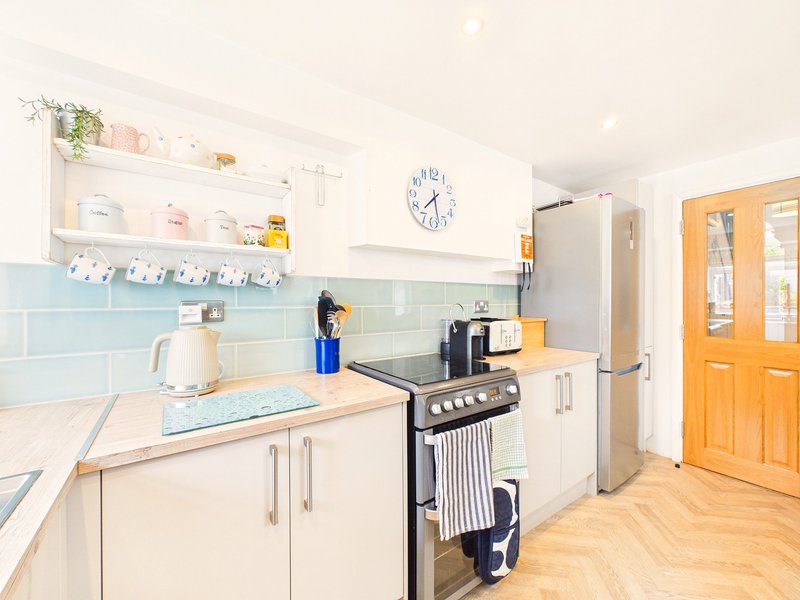 Bright kitchen with light blue tile backsplash, white cabinetry, black range cooker, and orange doors