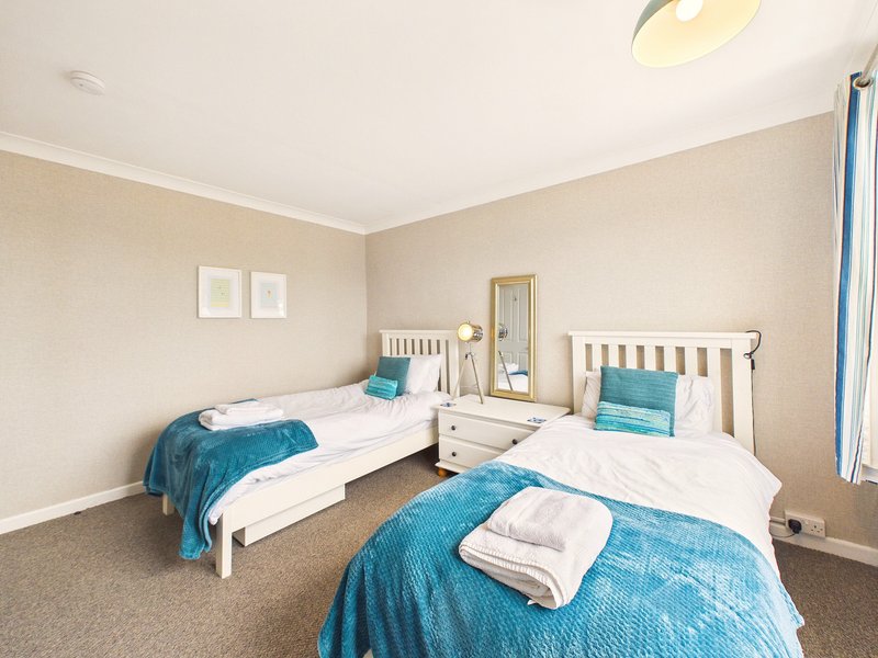 Bright bedroom with three single beds, white wooden frames, blue bedding, and neutral walls