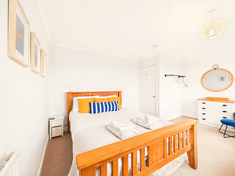Bright bedroom with wooden bed frame, white bedding, orange headboard, and neutral walls