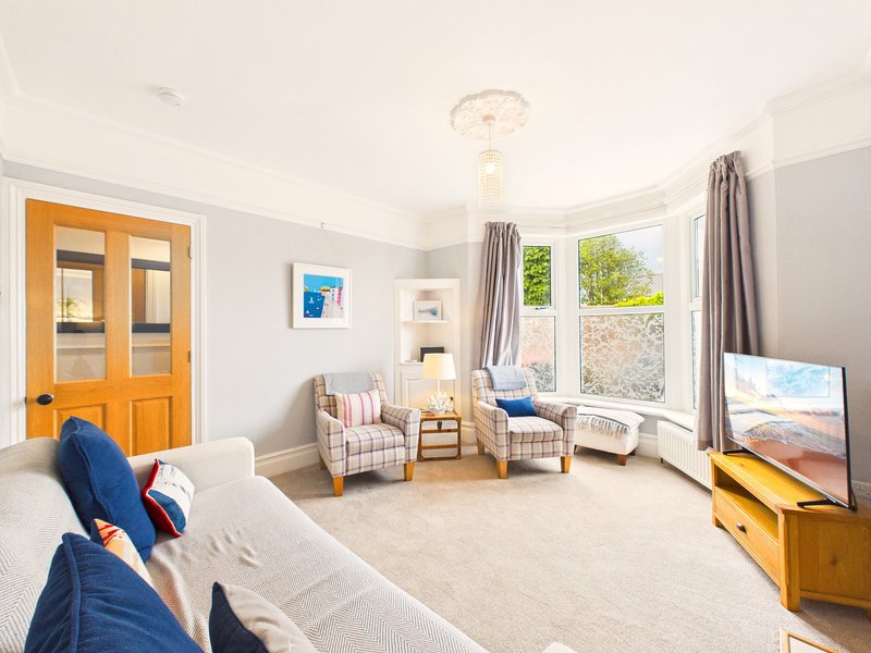Bright living room with cream sofa, patterned armchairs, wooden TV stand and large windows
