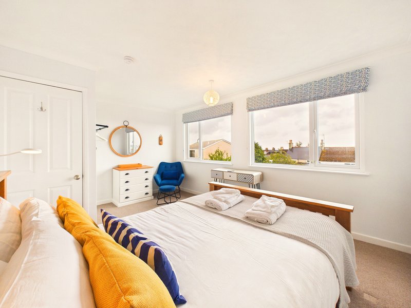 Bright bedroom with double bed, yellow and blue cushions, white furniture and large windows