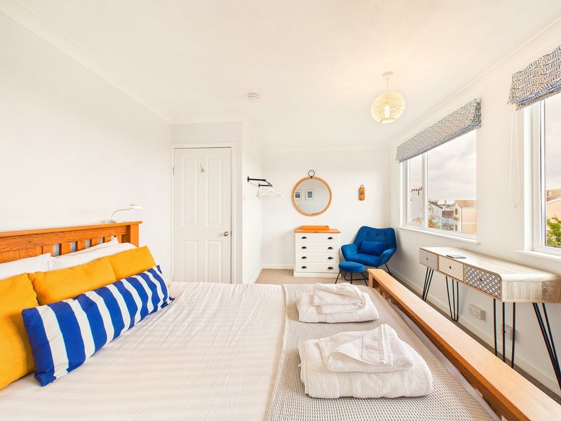 Bright bedroom with orange wooden bed frame, blue and white striped pillows, white bedding, and blue accent chair by window