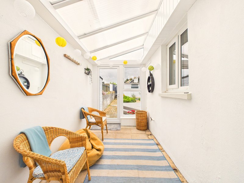 Bright sunroom with wicker furniture, blue striped rug, decorative mirror and hanging yellow ornaments