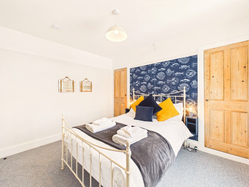 Bedroom with single bed, navy whale-patterned headboard, wooden wardrobe doors and ceiling light