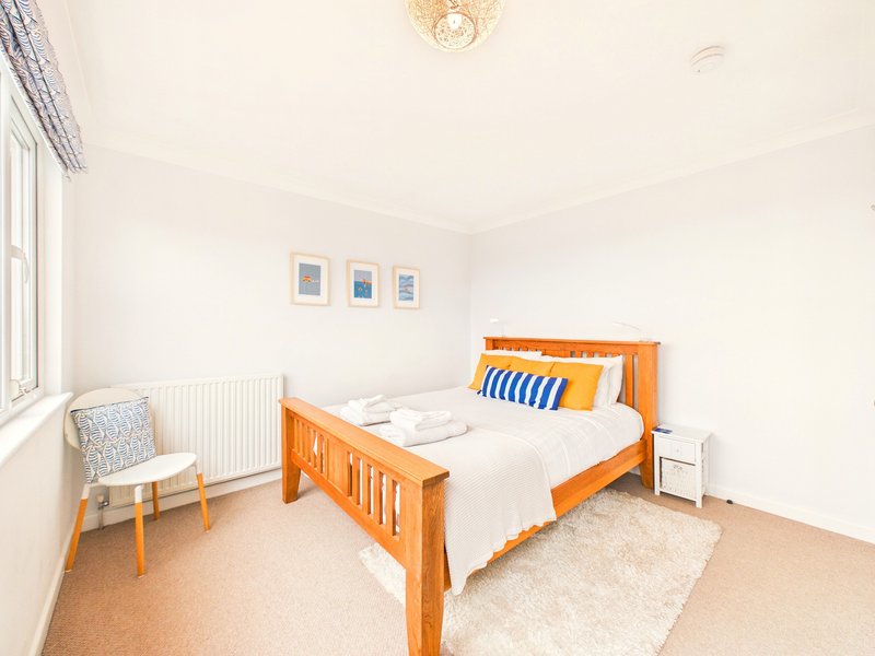 Bright bedroom with wooden bed frame, white bedding, small chair, and window