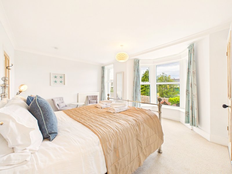 Bright bedroom with double bed, wooden floor, large windows and garden views