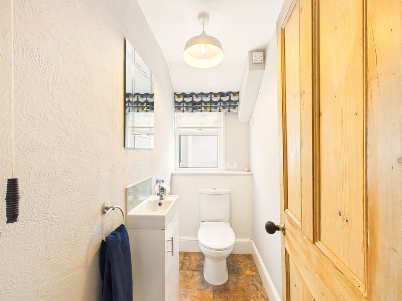Small bathroom with toilet, pedestal sink, mirror, window and wooden door