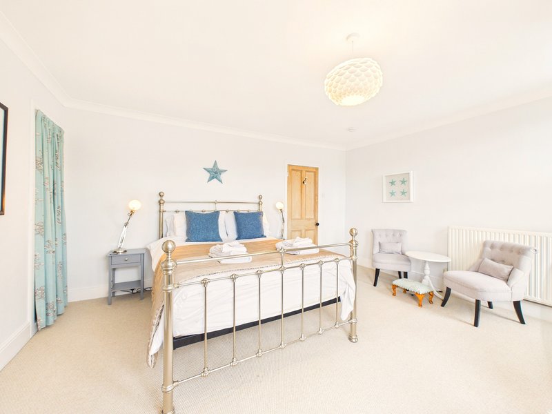 Bright bedroom with metal-framed bed, blue pillows, wooden nightstand, and seating area by window