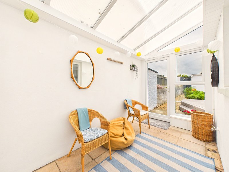 Bright conservatory with wicker chairs, wooden floor, blue striped rug and garden view