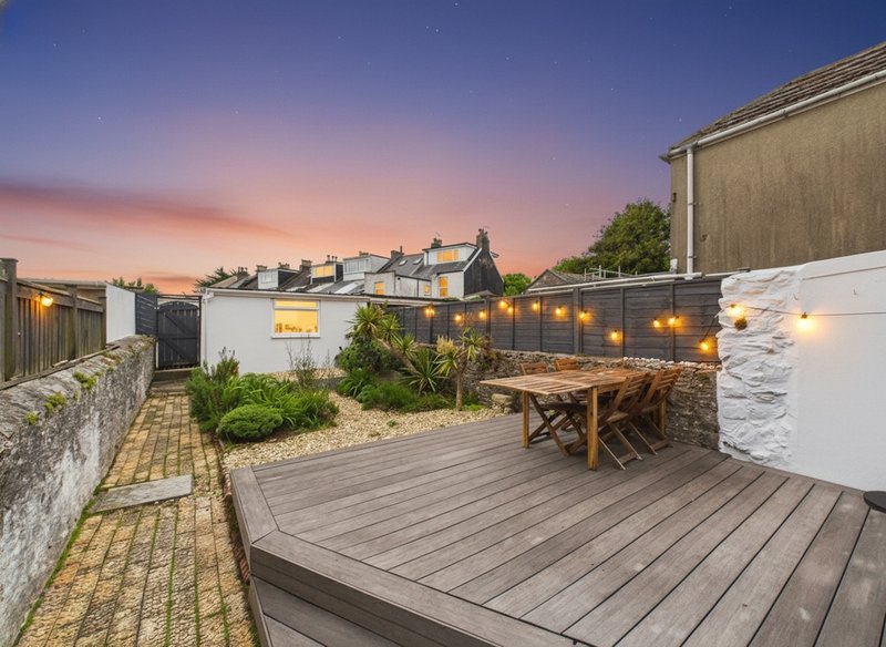 Rooftop terrace with wooden decking, dining table, string lights, and city views at dusk