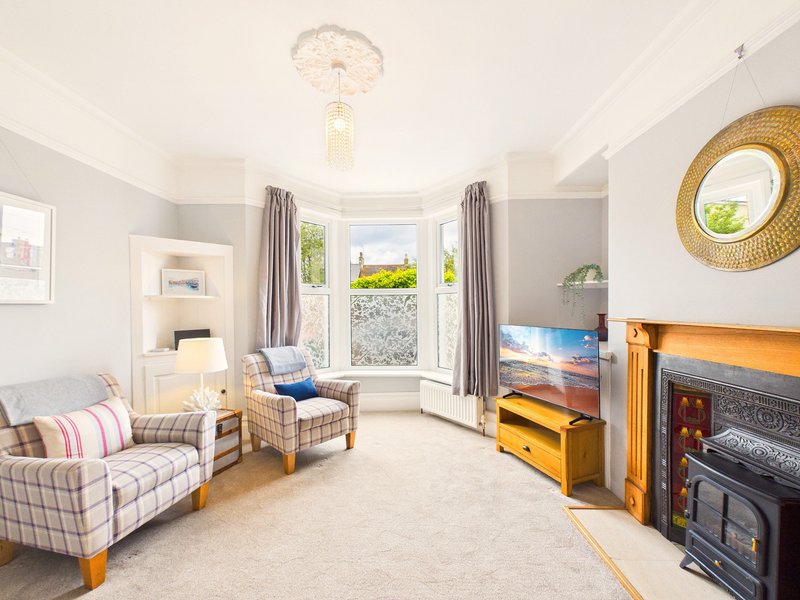 Bright living room with bay windows, fireplace, armchair, sofa and wooden furniture