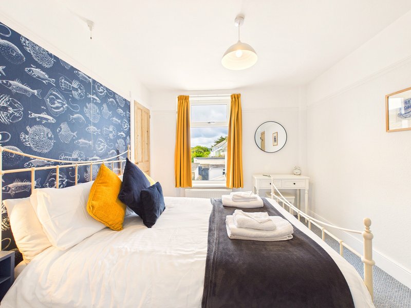 Bright bedroom with double bed, yellow and navy cushions, patterned headboard, window with yellow curtains