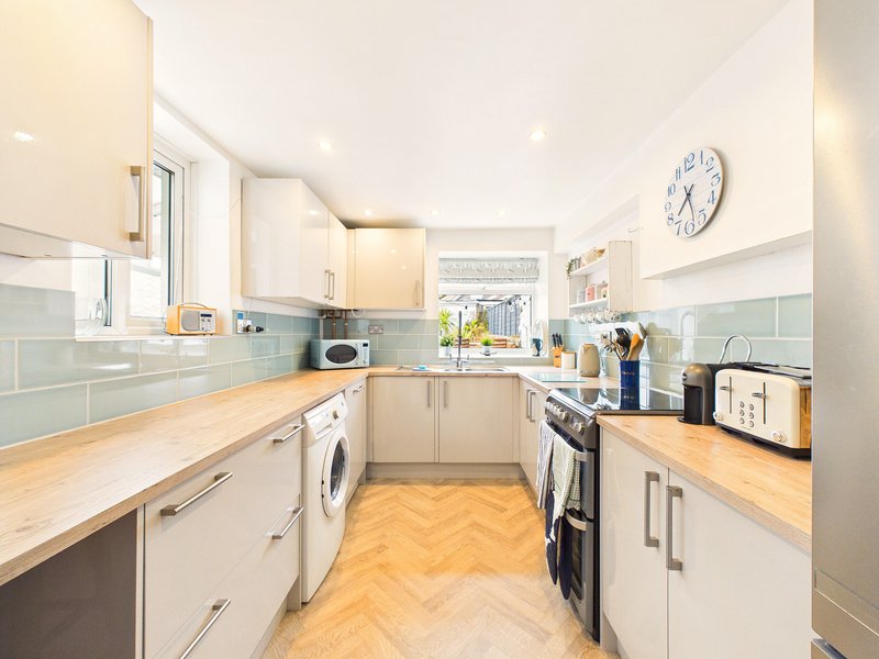 Modern galley kitchen with cream cabinets, wooden countertops, appliances and blue tile backsplash