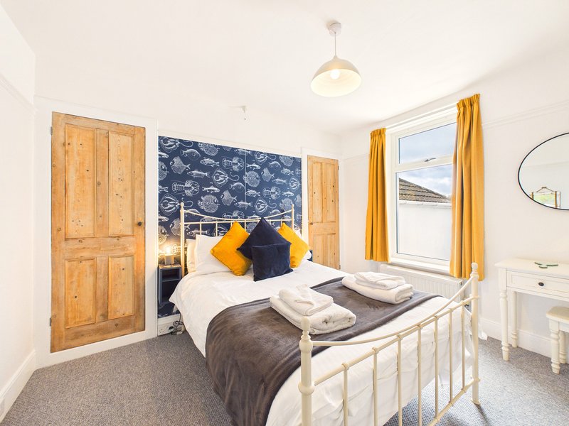Bright bedroom with single bed, wooden wardrobe, blue headboard, yellow curtains and window