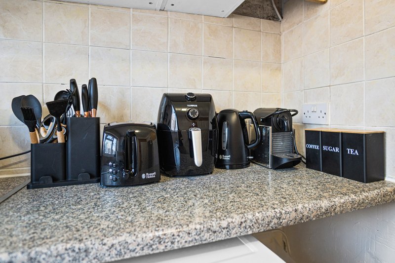 Kitchen countertop with black kitchen appliances, utensil holder, and tea storage box