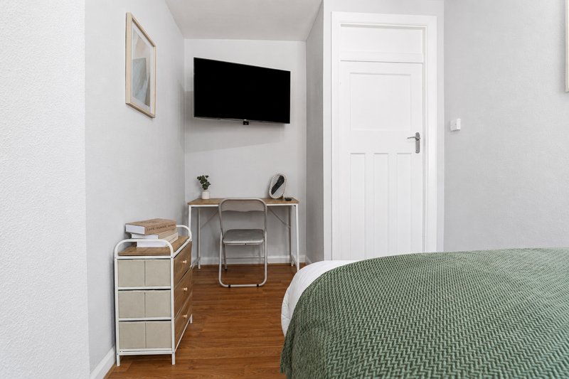Bedroom with double bed, wall-mounted TV, desk with chair, and wooden flooring