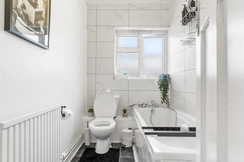 Compact bathroom with white tiles, toilet, sink, bathtub and window
