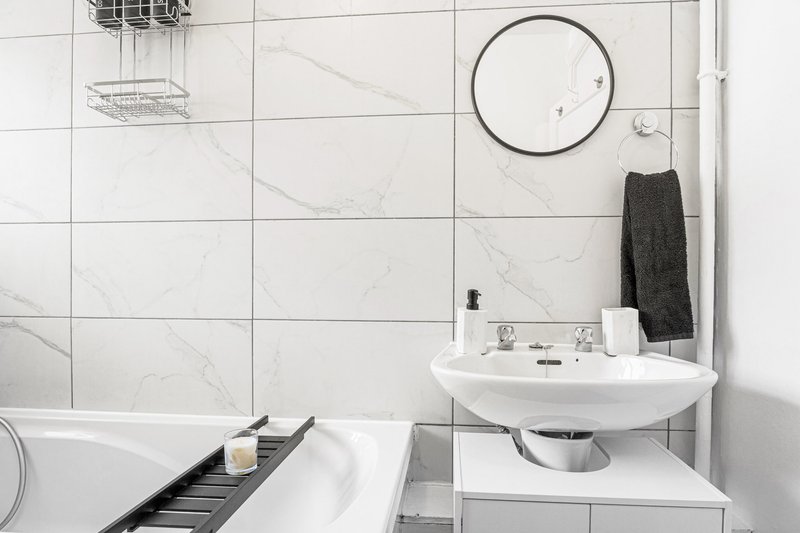 Modern bathroom with white marble-effect tiles, wall-mounted sink, circular mirror and bathtub