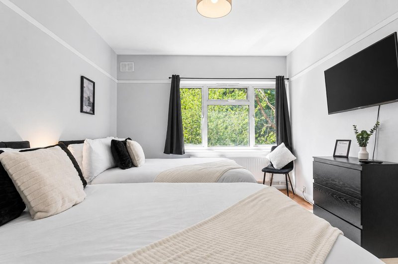 Modern bedroom with two beds, black furniture, wall-mounted TV, and garden view windows