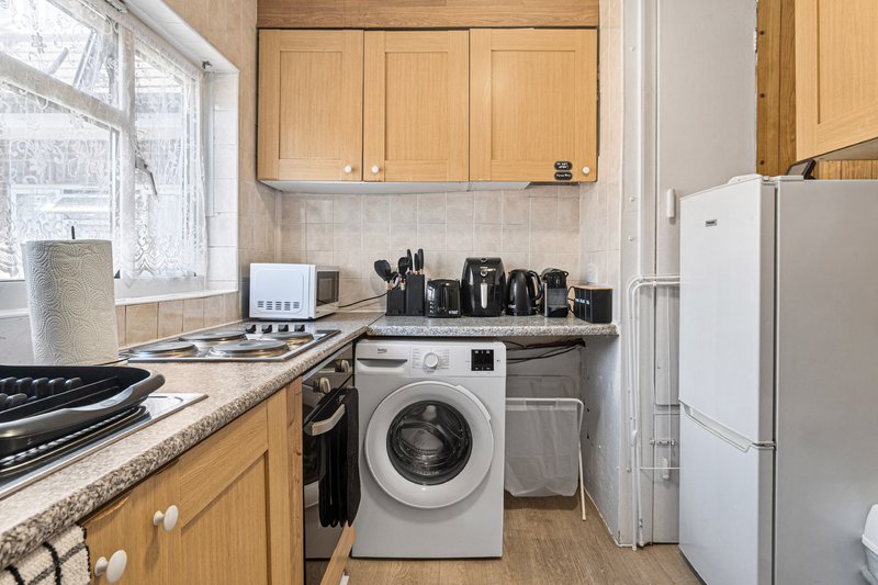 Kitchen with wooden cabinets, gas stove, washing machine, white fridge, and countertop appliances