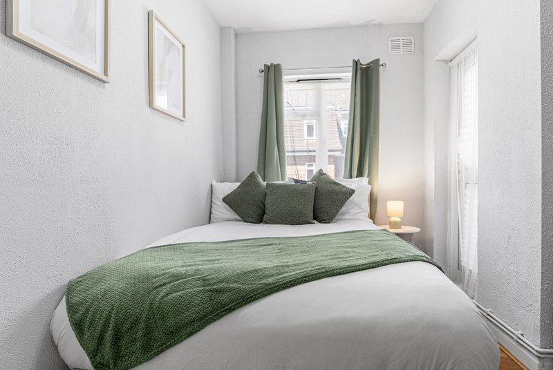 Bright bedroom with double bed, green bedding, cushions, and window with green curtains