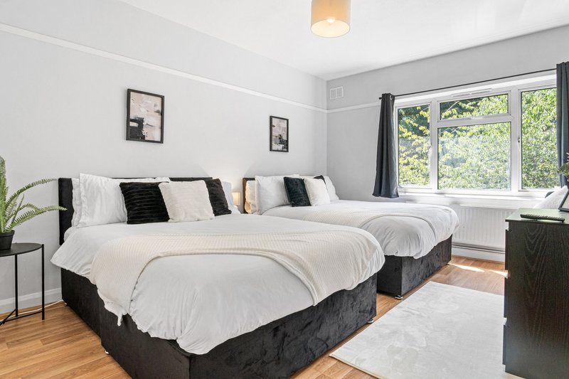 Bright bedroom with two single beds, white bedding, black headboards, wooden floor and large windows