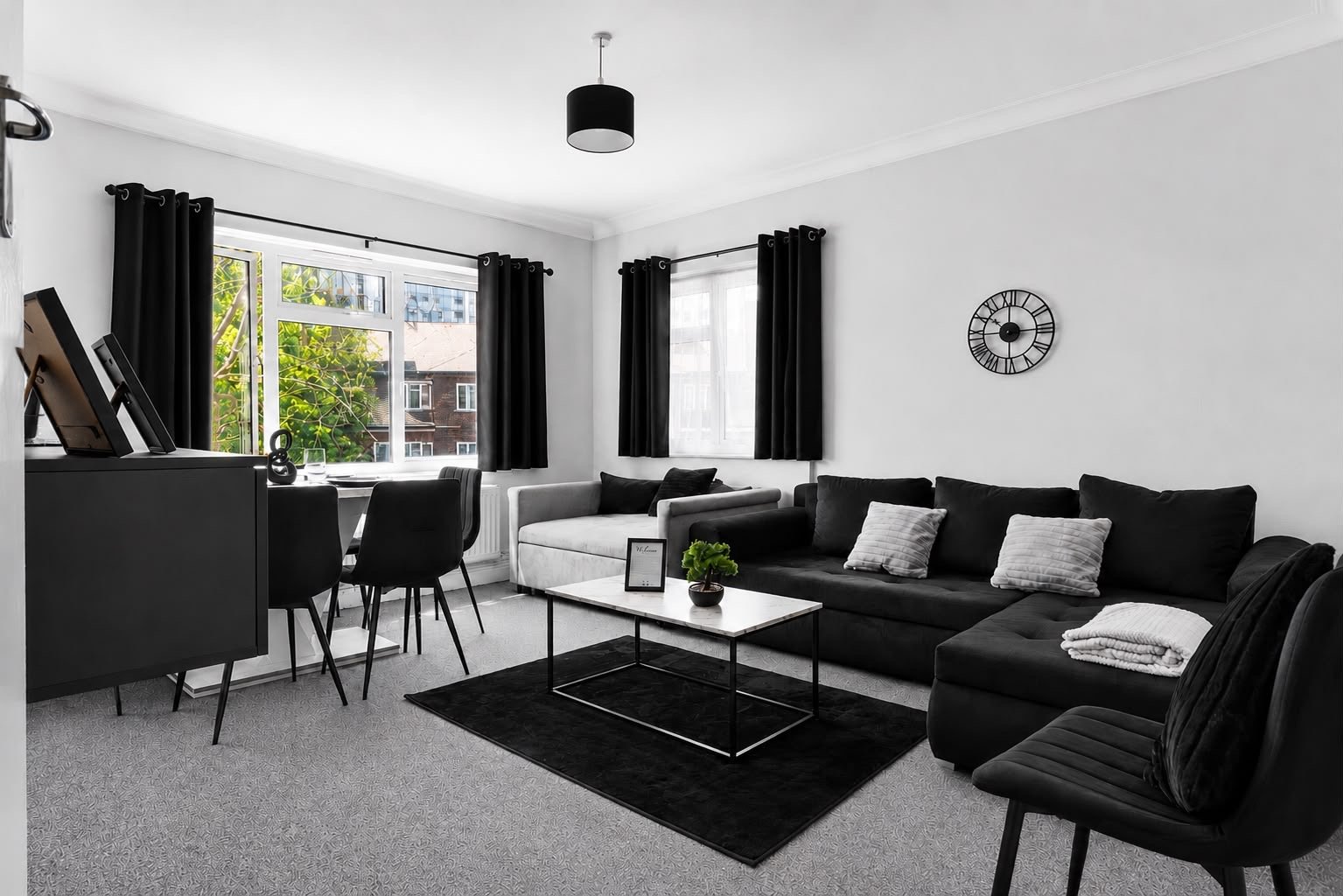 Modern living room with black sofa, armchair, coffee table and desk area by windows