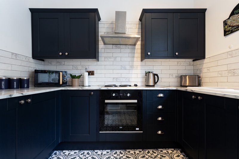 Modern kitchen with dark navy cabinets, white subway tile backsplash, stainless steel appliances and patterned floor