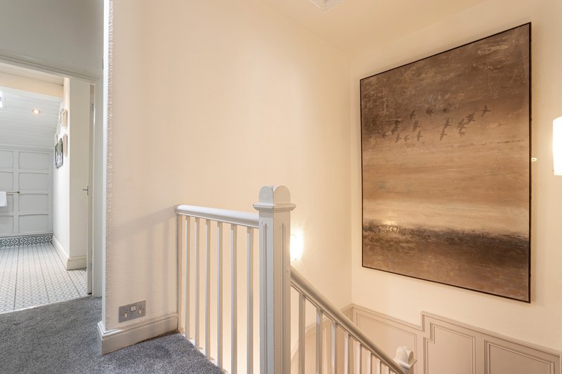 Landing area with white stair railing, framed abstract artwork, and open doorway to bathroom
