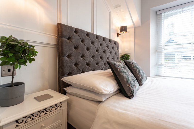 Modern bedroom with grey upholstered headboard, white bedding, decorative pillows and potted plant