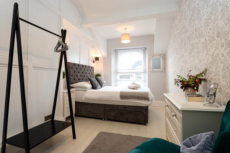 Modern bedroom with double bed, tufted headboard, clothing rack, and fresh flowers on dresser