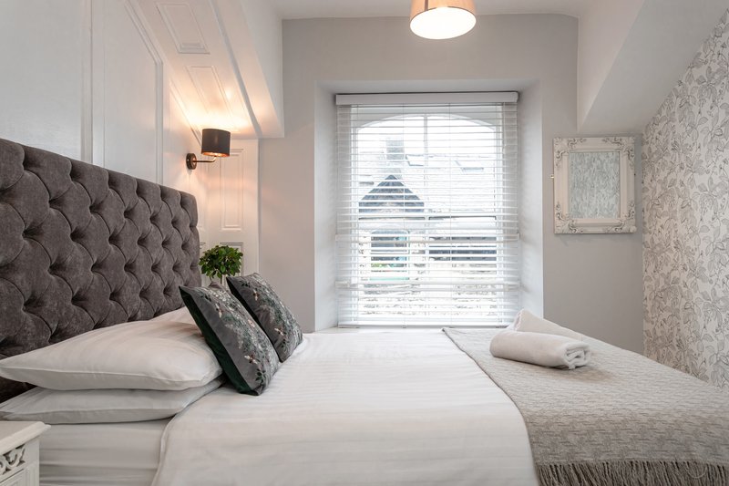 Modern bedroom with tufted headboard, white bedding, gray decorative pillows and pendant lighting