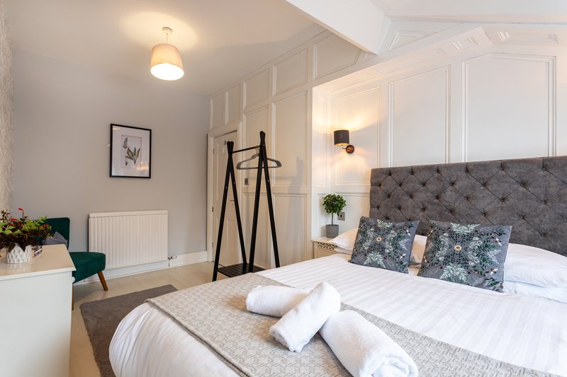 Modern bedroom with grey upholstered bed, white bedding, decorative pillows, and pendant lighting